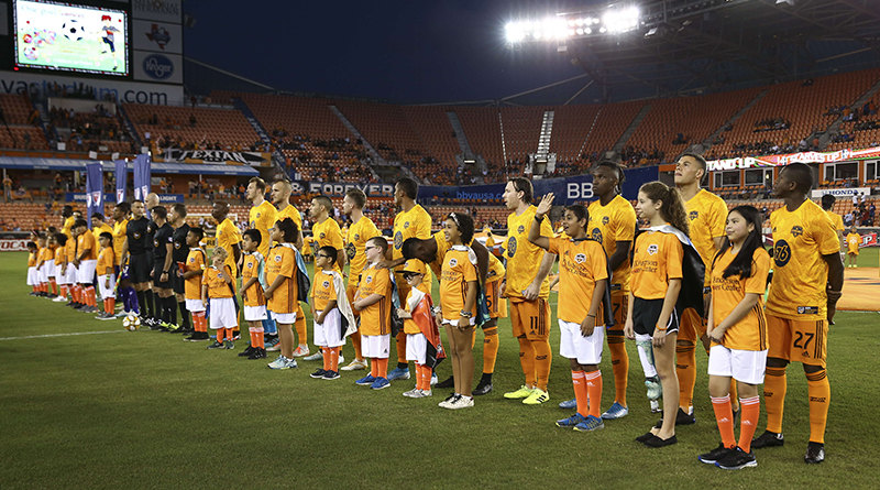 Houston Dynamo and Orlando City players stand on the field with children before a match at BBVA Stadium.