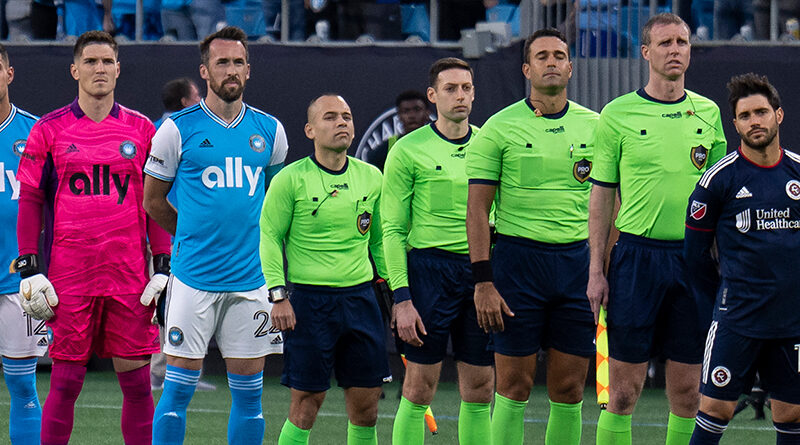 The officials line up with Charlotte FC and New England Revolution players during the national anthem before a game at Bank of America Stadium on March 19, 2022 in Charlotte, North Carolina. Steven Limentani/isiphotos.com