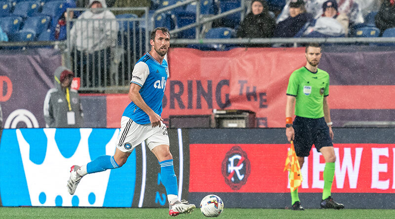 Christian Fuchs #22 of Charlotte FC brings the ball forward during a game between Charlotte FC and New England Revolution at Gillette Stadium on April 16, 2022 in Foxborough, Massachusetts, watched by PRO AR Kyle Atkins. Andrew Katsampes/ISI Photos.